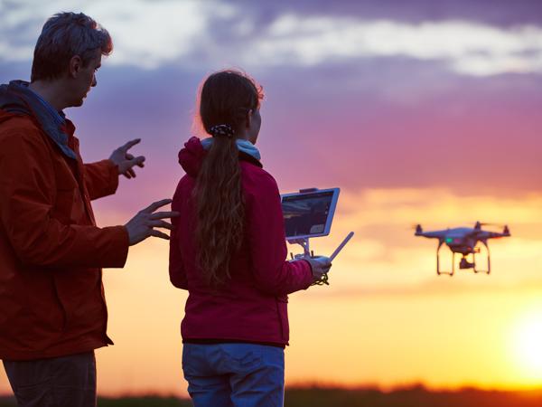 A father and daughter flying a drone together at sunset