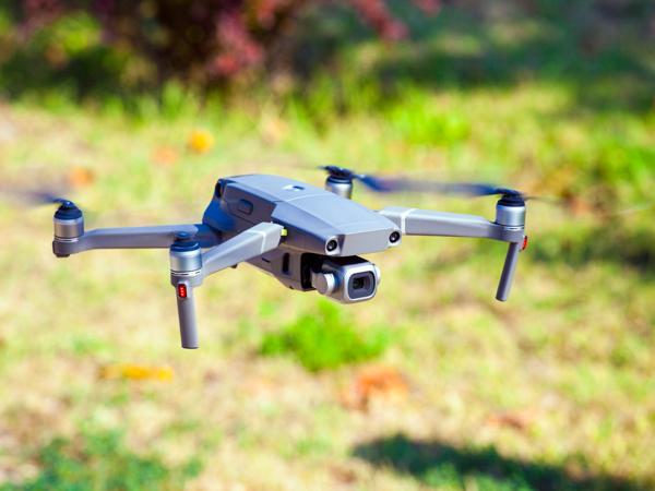 A small folding camera drone hovering low over a grassy field